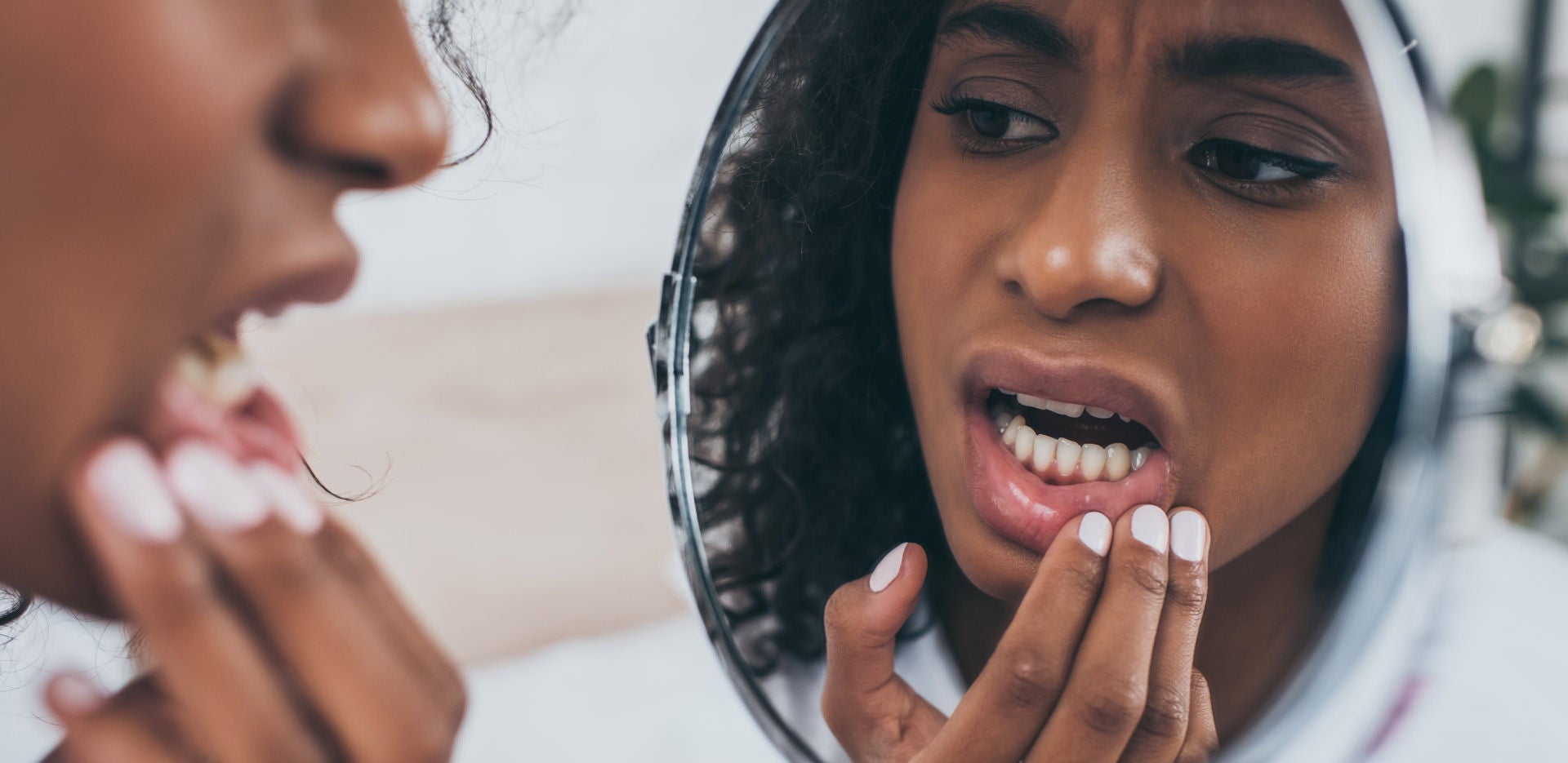 Jeune femme afro-américaine se regardant dans le miroir, souffrant d'une douleur dentaire.