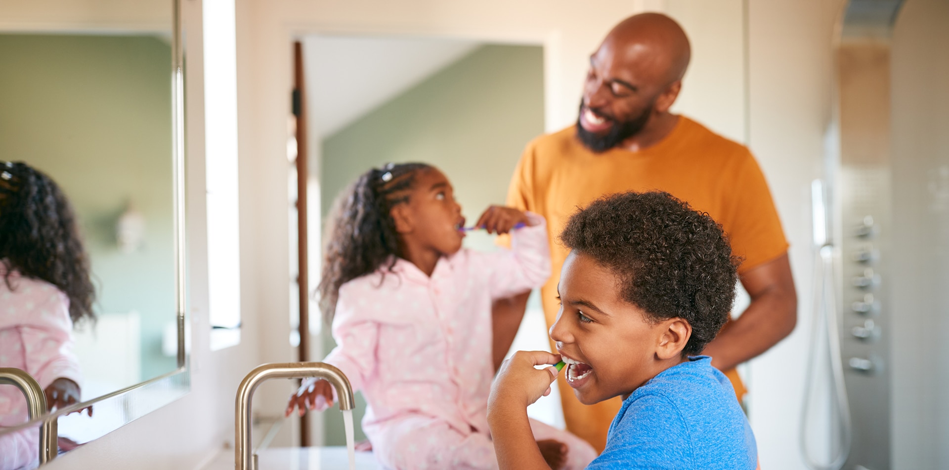 Father Helping Children To Brush Teeth In Bathroom At Home