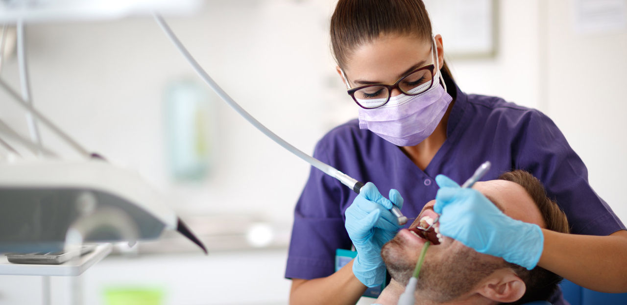 Young female dentist drilling tooth to patient